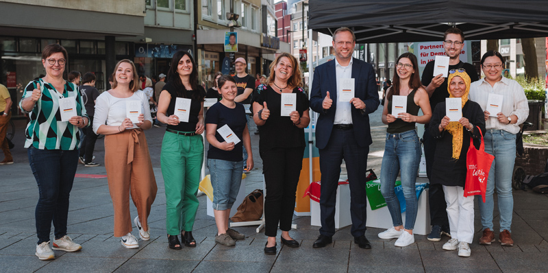 Mitarbeiterinnen und Mitarbeiter der Stadt Ulm sowie von "Jugend aktiv" präsentieren in der Fußgängerzone kleine Bücher mit dem Grundgesetz.